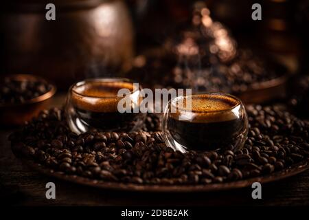 Espresso in una tazza di vetro a doppia parete su fondo chicchi di caffè, immagine dai toni scuri Foto Stock