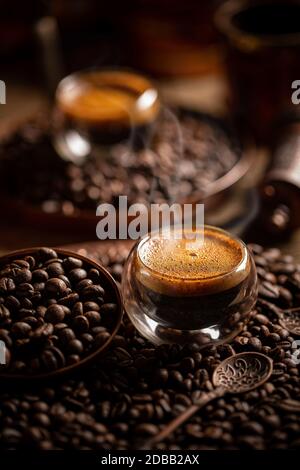 Espresso in una tazza di vetro a doppia parete su fondo di chicchi di caffè tostati Foto Stock