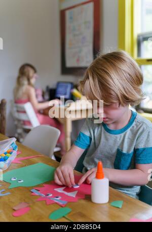 Ragazzo (4-5) che prepara il taglio di carta, ragazza (6-7) in background Foto Stock