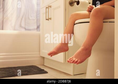 Gambe di bambina (2-3) seduta sul sedile wc Foto Stock