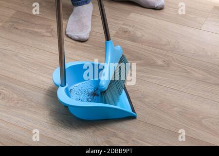 L'uomo spazza i detriti in una paletta blu con una spazzola. Foto Stock