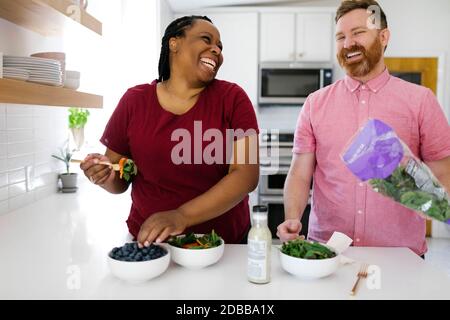 Felice uomo e donna che prepara insalata in cucina Foto Stock