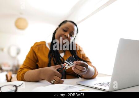 Donna tagliando carta di credito con forbici mentre lavora a casa ufficio Foto Stock