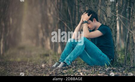 L'uomo infelice nella foresta soffre di depressione e frustrazione della vita. Foto Stock