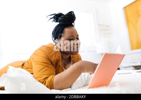 Donna sorridente sdraiata a letto e che usa la tavoletta Foto Stock