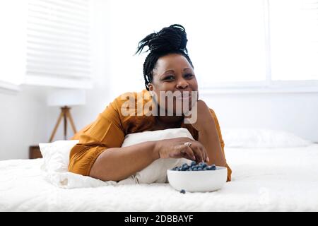 Donna sdraiata a letto, mangiando mirtilli e guardando la tv Foto Stock