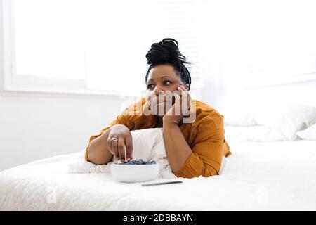 Donna sdraiata a letto, mangiando mirtilli e guardando la tv Foto Stock