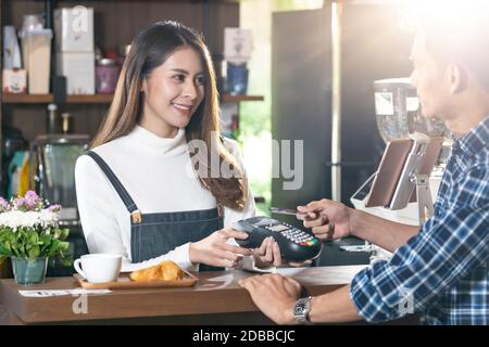 I clienti asiatici che utilizzano la tecnologia nfs con carta di credito contactless pagano al barista al bar. Pagamento senza contatto che impedisce il coronavirus covid-19 Sprea Foto Stock