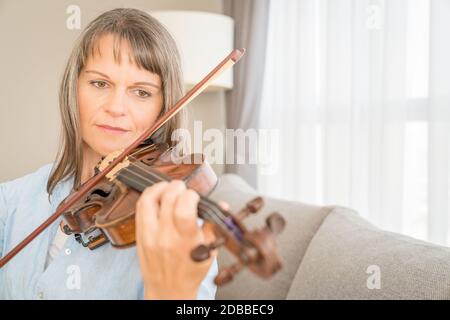 Donna matura che gioca violino nel suo appartamento urbano Foto Stock