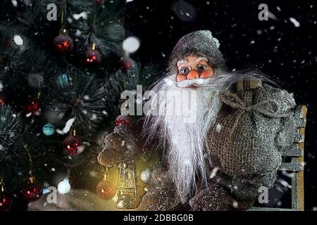 Santa Claus all'esterno accanto all'albero di Natale in nevicata portando doni ai bambini. Buon Natale & Capodanno concept Foto Stock