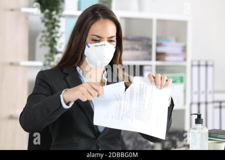 Donna executive con maschera protettiva che rompe contratto su una scrivania in ufficio Foto Stock