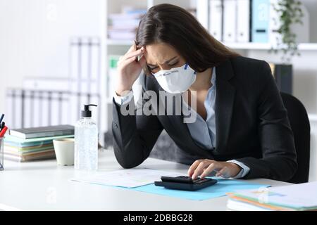 Bookkeeper preoccupato con maschera protettiva che guarda la calcolatrice su una scrivania in ufficio Foto Stock