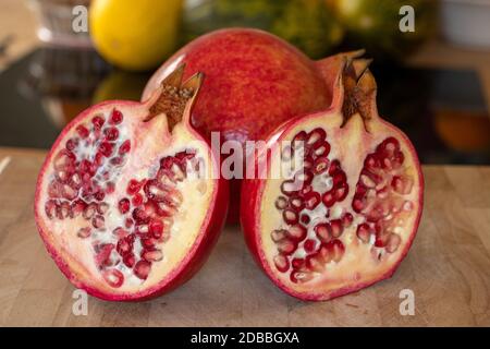 Primo piano di una frutta intera e due metà melograni su un tagliere in legno in una cucina domestica Foto Stock