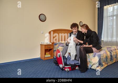 Felice giovane famiglia con valigie si siede nel letto. Vacanza. Foto Stock