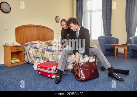 Felice giovane famiglia con valigie si siede nel letto. Vacanza. Foto Stock