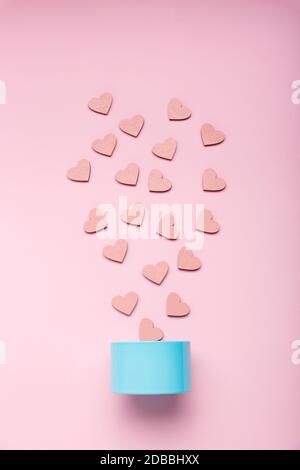 Scatola regalo in metallo e cuori decorativi rosa che cadono su uno sfondo rosa. Vista dall'alto Foto Stock