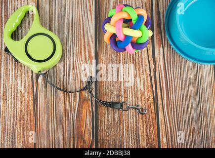 Concetto di accessori per animali domestici. Guinzagli con giocattolo in gomma e ciotola su sfondo di legno. Foto Stock