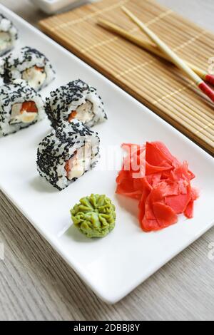 Minimalismo e raffinatezza: Delizioso sushi di salmone e avocado ricoperto di semi di sesamo nero. Servito con zenzero e wasabi su un piatto bianco. Ver Foto Stock