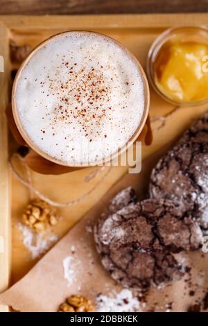 Tazza di caffè con schiuma aromatica e cannella, biscotti e marmellata su sfondo rustico. Vista dall'alto. Messa a fuoco selettiva, primo piano. Foto per pubblicità o b Foto Stock