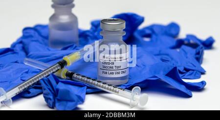 Un paio di flaconcini per vaccino di prova Covid-19 sopra i guanti per uso medico in gomma blu. Foto Stock