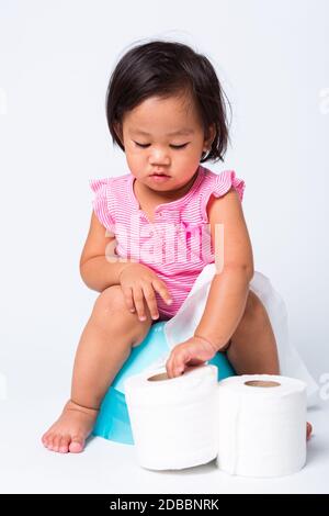 Asiatico poco cute bambino ragazza formazione di formazione a sedersi su piatto blu camera o vasino con carta igienica rotoli, studio girato isolato su bianco ba Foto Stock