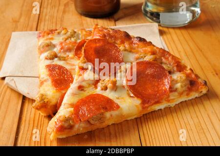 Fette di pepperoni e pizza di salsiccia su legno rustico tavolo con birra Foto Stock