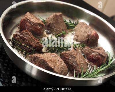 Filetto di manzo biologico con rosmarino fresco e timo in una padella di acciaio inossidabile, vista dall'alto, cucina con erbe fresche, cibo biologico o cibo sano Foto Stock