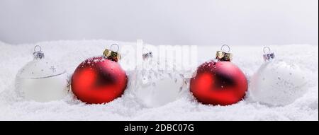 Natale bordo di rosso e bianco baubles ornamenti nella neve su sfondo chiaro Foto Stock