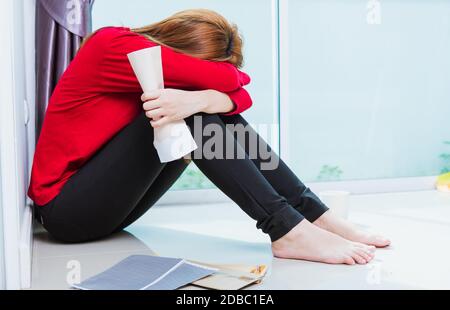 Asian giovane donna triste abbracciare il suo ginocchio e gridare indossando maschera facciale protettiva disoccupato quarantine malattia coronavirus o COVID-19 sua seduta da sola su fl Foto Stock