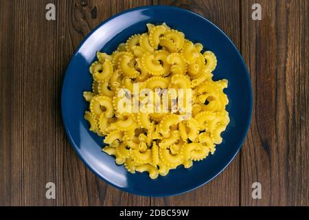 Pasta di Pene lisce in piatto blu su fondo di legno scuro. Viste dall'alto. Foto Stock