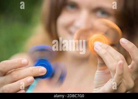 Giovane bella bruna ragazza sorride e si stolge intorno con il movimento gli spinner in mano in estate Foto Stock