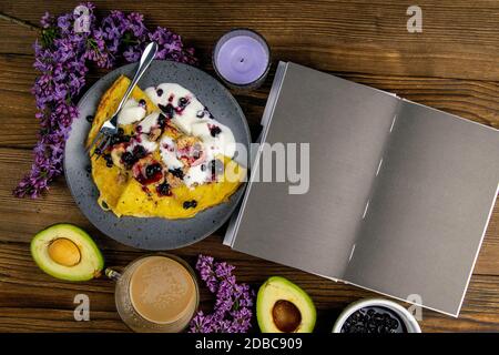 Pancake con frutti di bosco e banane su un piatto grigio con blocco note vuoto su sfondo di legno scuro, vista dall'alto. Da sopra, posa piatta, in alto. Foto Stock