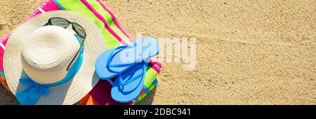 Telo da spiaggia con cappello, occhiali da sole e infradito fotografato dall'alto sulla spiaggia di sabbia, caldi accessori estivi, destinazione di vacanza Foto Stock