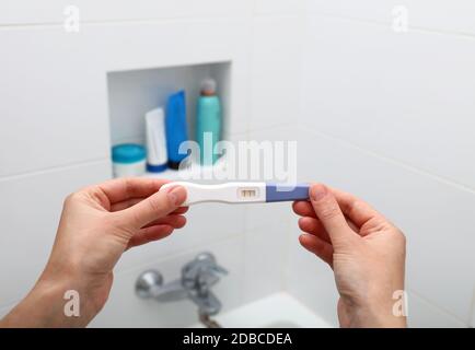 Primo piano donna mani tenendo test di gravidanza positivo in bagno, prospettiva personale, vista ad alto angolo Foto Stock