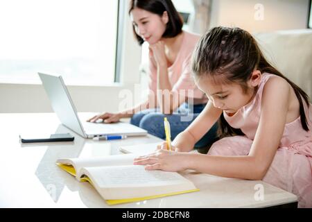 madre che lavora a casa e figlia di aiuto che fa lavoro a casa Foto Stock