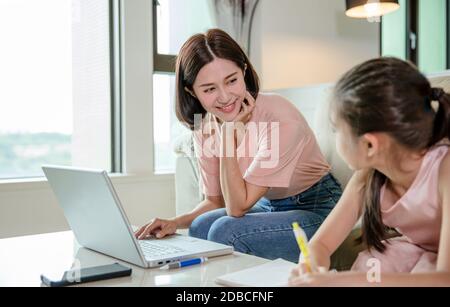 madre che lavora a casa e figlia di aiuto che fa lavoro a casa Foto Stock