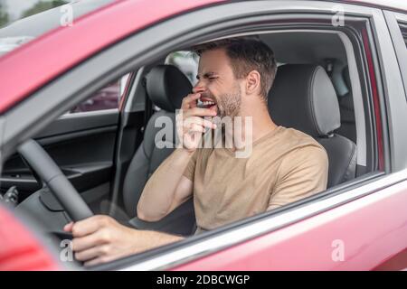 Stanco giovane maschio che guida auto rossa, sbadigli Foto Stock