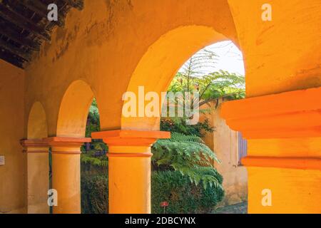 Soleggiato tardo pomeriggio in un palazzo mediterraneo. Pareti color ocra brillante, archi graziosi, siepi verdeggianti. Foto Stock