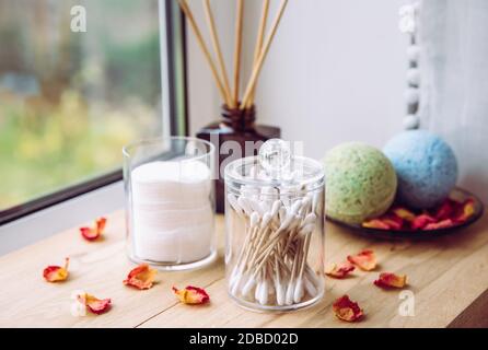 Davanzale in legno naturale per il bagno con imbottiture in cotone impilate, Q-Tips all'interno dei contenitori organizzativi. Tamponi in cotone impilati, puntali Q-Tips. Flacone diffusore di liquido. Foto Stock