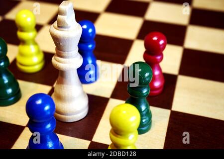 concetto di scacchi alla diversificazione, pegni colorati huddle intorno al grande vecchio re bianco Foto Stock