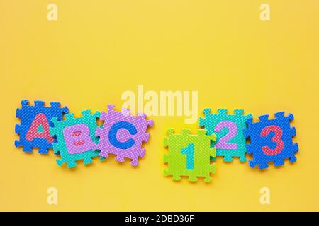 Alfabeto puzzle con numero puzzle su sfondo giallo. Vista superiore Foto Stock