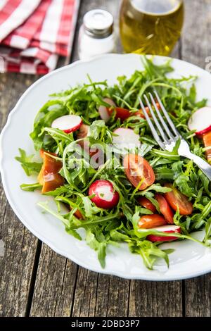 Insalata di rucola fresca con ravanelli, pomodori e peperoni rossi sul piatto. Foto Stock