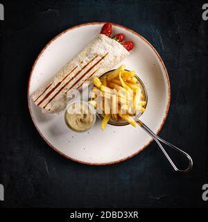 Piatto di tortilla con salsicce alla griglia con patatine fritte e salsa all'aglio su sfondo scuro Foto Stock
