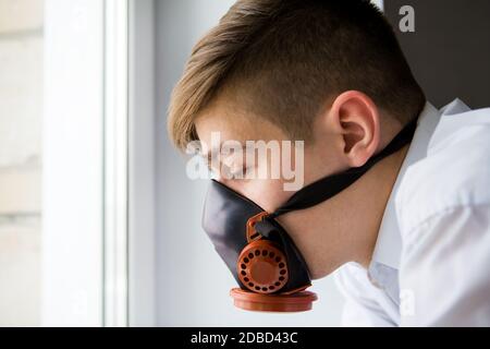 Uomo giovane triste in una maschera a gas vicino alla finestra In camera Foto Stock