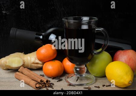 Un bicchiere di VIN brulé con ingredienti. Radice di zenzero, cannella tubes, chiodi di garofano, mela e mandarino su sfondo sfocato. Messa a fuoco selettiva. Foto Stock