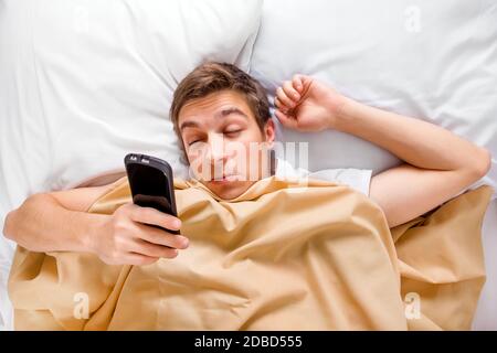 Stanco e Sleepy giovane uomo svegliarsi con un telefono Nel letto Foto Stock