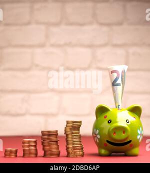 Sorridente verde Piggy banca con monete e banconote impilate, concetto di crescita finanziaria Foto Stock