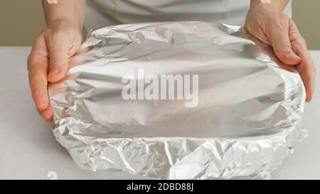 Lo chef avvolge la teglia da forno con un foglio di alluminio. Cottura Foto Stock