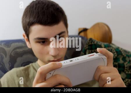 Il ragazzo caucasico gioca con una console portatile sul divano Foto Stock