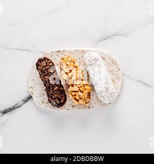 Set di tre eclair fatti in casa su sfondo marmoreo. Vista dall'alto di deliziosi profittole salutari con diversi ingredienti di arredamento - cioccolato, arachidi e. Foto Stock